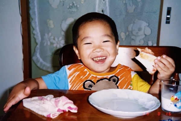 レトロなフィルム写真。朝ごはんを手づかみで食べながら笑う男の子